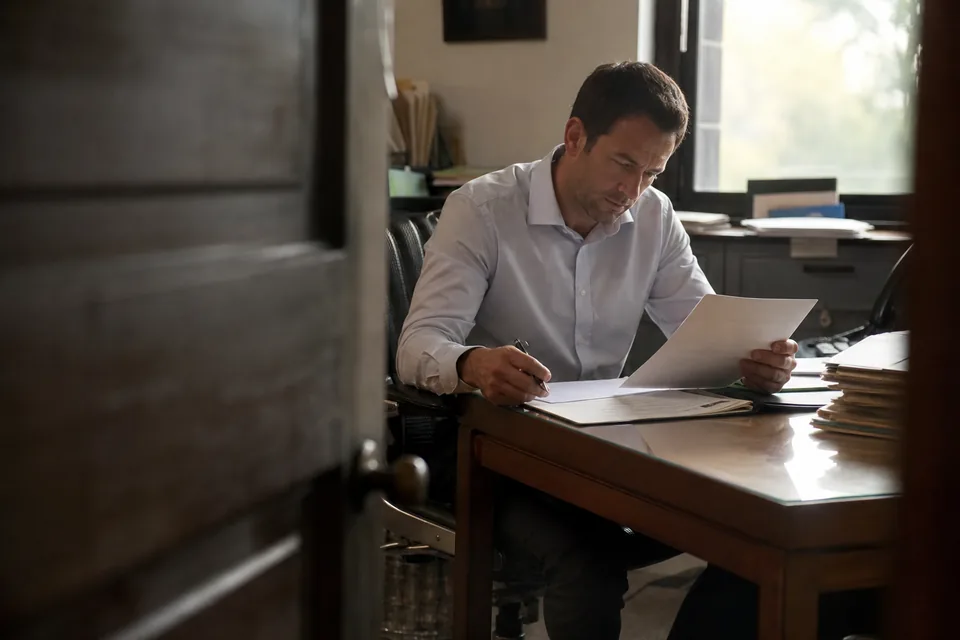 Kierownik finansowy czyta pismo przy biurku, obok leży lista kontrolna i długopis